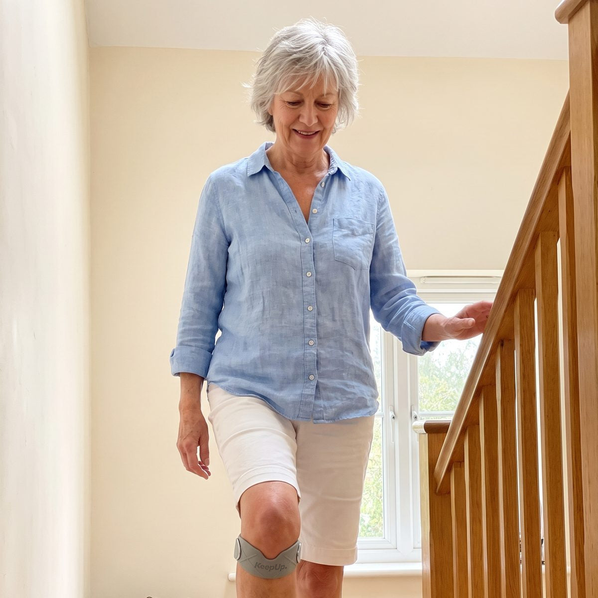 A woman in her sixties walking down her stairs at home with a grey strap just under her kneecap