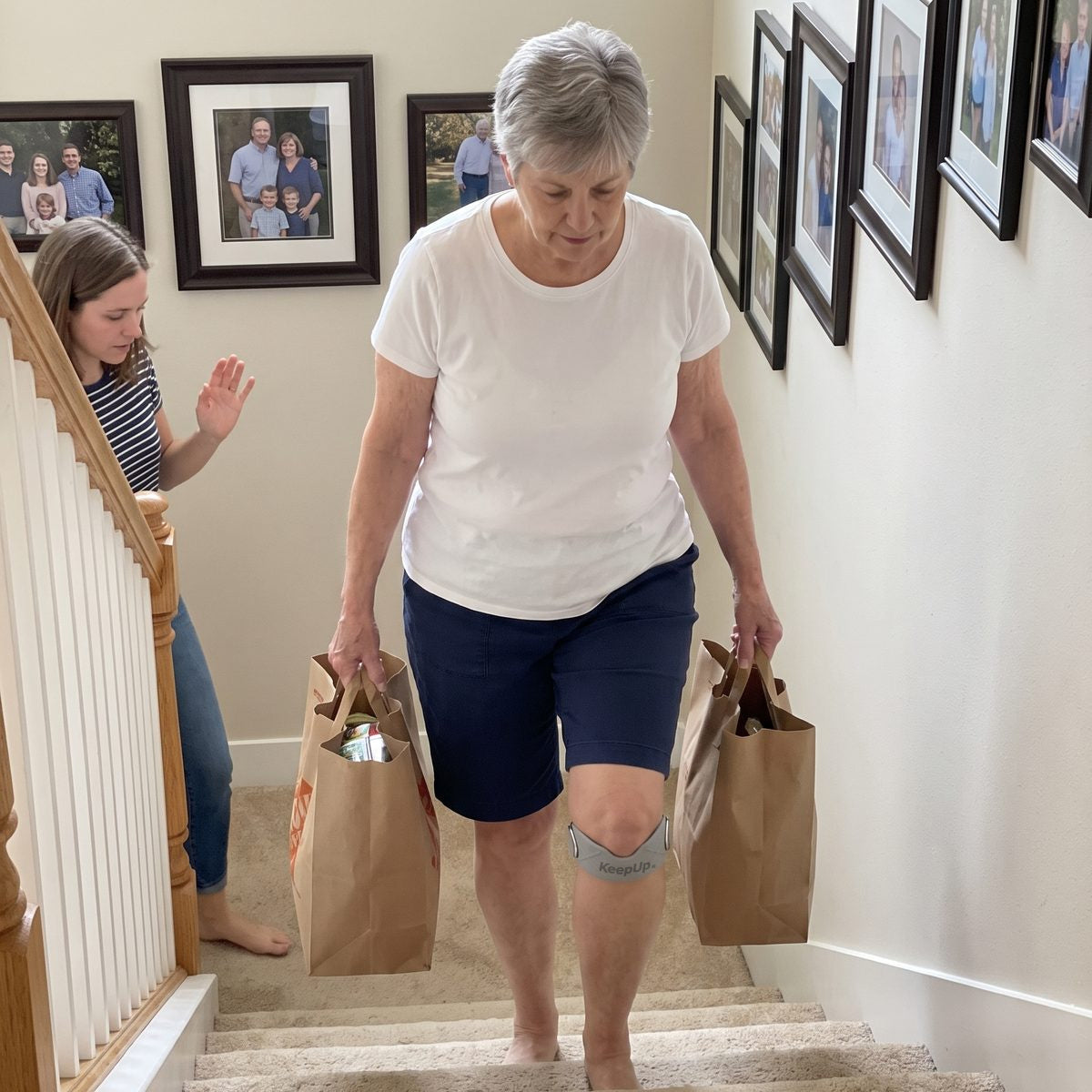 A woman in her sixties carrying two grocery bags up the stairs, her daughter behind her