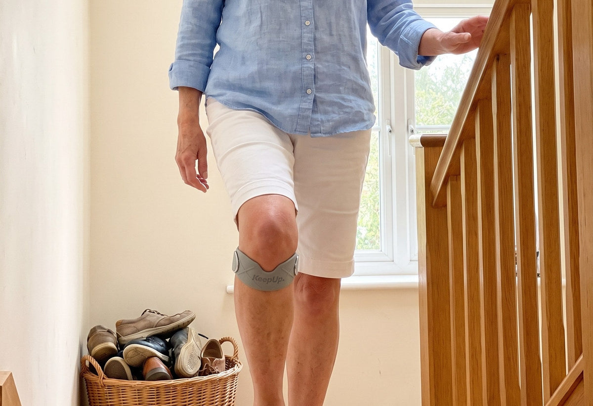 A woman in her sixties walking down her stairs at home, wearing the grey KeepUp strap just under her kneecap